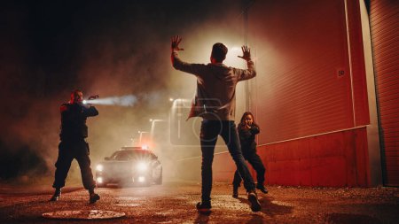 Photo for Two Police Officers Aim at a Fellon. Cops Using a Weapon to intimidate the Suspect. Fellon Raising Hands in Compliance. Heroic Law Enforcement - Royalty Free Image