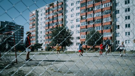 Kinder aus der Nachbarschaft spielen draußen im städtischen Hinterhof Fußball. Junger Fußballspieler macht einen Strafstoß. Multikulturelle Freunde spielen gemeinsam Fußball