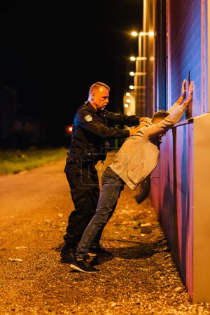 Photo for A Professional Middle Aged Policeman Performing a Pat-Down Search on a Fellon in Empty Back Alley. Documentary-like Shot of Proper Procedure of - Royalty Free Image
