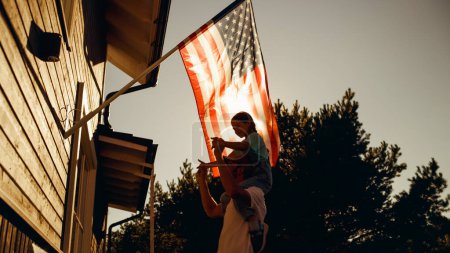 Foto de Happy Patriotic Dad Holding His Young Daughter of His Shoulders, Helping Her to Put the United States of America Flag on the Wall of Their House to - Imagen libre de derechos