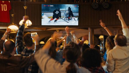 Eine Gruppe von Freunden verfolgt ein Live-Eishockeyspiel im Fernsehen in einer Sportsbar. Aufgeregte Fans jubeln und schreien. Junge Leute feiern, wenn die Mannschaft punktet