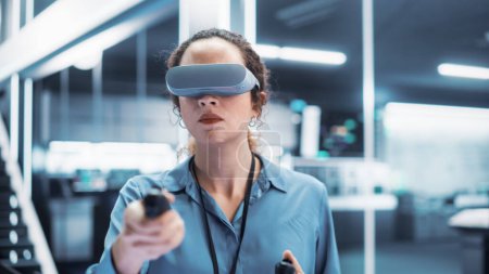 Portrait of a Female Engineer Using a Virtual Reality Headset with Controllers to Operatean Indsutrial Robot or Spend Time in Virtual Office Metaverse