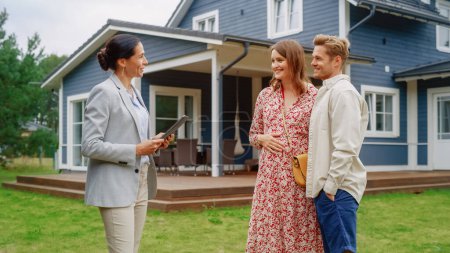 Photo for Young Couple Visiting a Potential New Home Property with Professional Real Estate Agent. Female Realtor Showing the House to Future Homeowners. Focus - Royalty Free Image