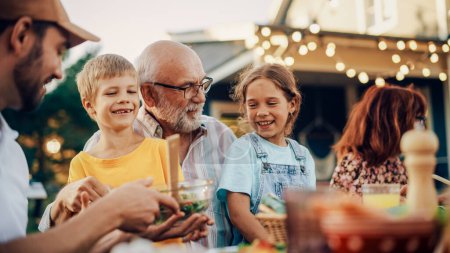 Heureux grand-père aîné parlant et s'amusant avec ses petits-enfants, les tenant sur le tour lors d'un dîner en plein air avec de la nourriture et des boissons. Adultes à un