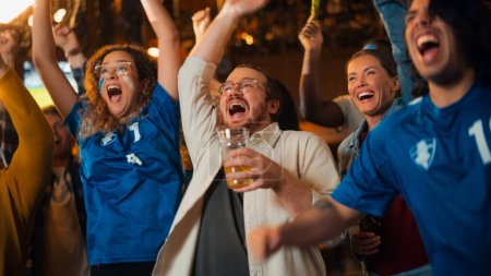 Group of Soccer Fans with Colored Faces Watching a Live Football Match in a Sports Bar. People Cheering for Their Team. Player Scores a Goal and Crowd