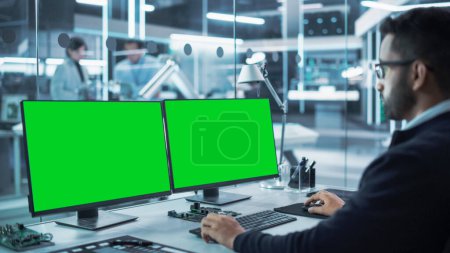 Développeur de logiciels travaillant sur un ordinateur de bureau avec deux écrans d'affichage Chromakey d'écran vert dans une usine. Recherche technologique moderne