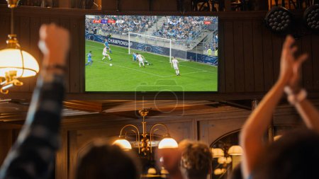 Group of Friends Watching a Live Soccer Match on TV in a Sports Bar. Excited Fans Cheering and Shouting. Young People Celebrating When Team Scores a
