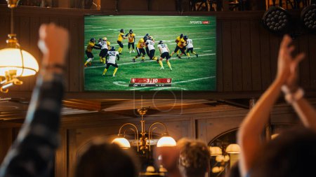 Gruppe von American-Football-Fans, die eine Live-Übertragung eines Spiels in einem Sport-Pub im Fernsehen verfolgen. Menschen jubeln, unterstützen ihr Team. Menschenmenge wird ekstatisch