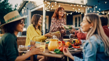 Famille et amis multiethniques divers se réunissant à une table de jardin. Les gens mangent des légumes grillés et frais, partageant des salades savoureuses pour un