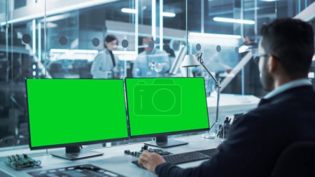 Ingénieur industriel travaillant sur un ordinateur de bureau avec deux écrans d'affichage Chromakey à écran vert dans une recherche et un développement technologiques modernes