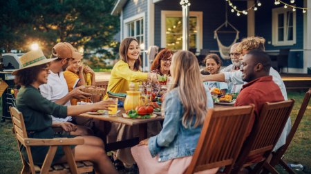 Famille et amis multiethniques divers se réunissant à une table de jardin. Les gens mangent des légumes grillés et frais, partageant des salades savoureuses pour un