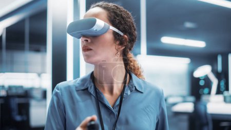 Portrait d'une ingénieure utilisant un casque de réalité virtuelle avec des contrôleurs pour faire fonctionner un robot industriel ou passer du temps dans une métaverse de bureau virtuel