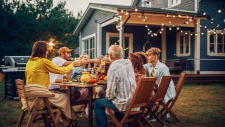 Famille et amis multiethniques divers se réunissant à un dîner de table de jardin. Les personnes âgées et les jeunes Toasting et clinking verres avec frais