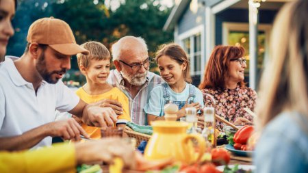 Portrait d'un grand-père aîné heureux tenant ses petits-enfants brillants et talentueux sur le tour lors d'un dîner en plein air avec de la nourriture et des boissons. Famille