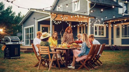 Photo for Parents, Children and Friends Gathered at a Barbecue Dinner Table Outside a Beautiful Home. Multicultural Old and Young People Have Fun, Eat and Drink - Royalty Free Image