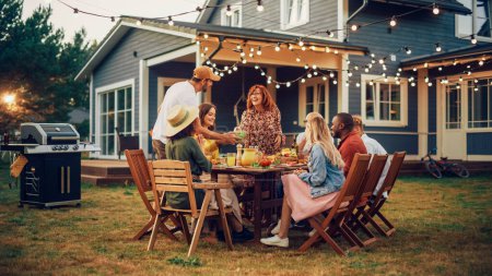 Parents, enfants et amis se sont réunis à une table de barbecue à l'extérieur d'une belle maison. Les personnes âgées et les jeunes s'amusent, mangent et boivent. Fête de jardin