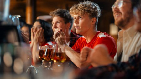 Group of Young Friends Watching a Live Soccer Match on TV in a Sports Bar. Excited Fans Cheering and Shouting. Young People Celebrating When Team