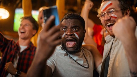 Porträt zweier aufgeregter Freunde, die ein Smartphone in der Hand halten, feiern den Gewinn einer Sportwette auf ihre Lieblingsfußballmannschaft. Lebhafte, erfolgreiche Emotionen