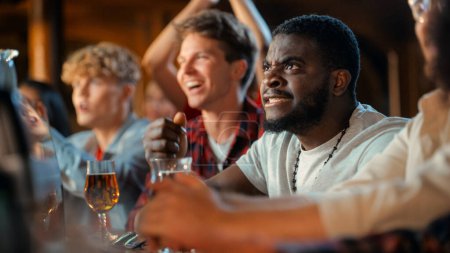 Nervous African Man Watching a Live Soccer Match on TV in a Sports Bar. Excited Fans Cheering and Shouting. Young Black Male Stress Out for His Team