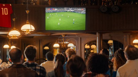 Group of Soccer Fans Watching a Live Football Match Broadcast in a Sports Pub on TV. People Cheering, Supporting Their Team. Crowd Goes Ecstatic When