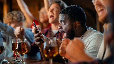 Stressed African Man Watching a Live Soccer Match on TV in a Sports Bar. Excited Fans Cheering and Shouting. Young Black Male Nervous for His Team at