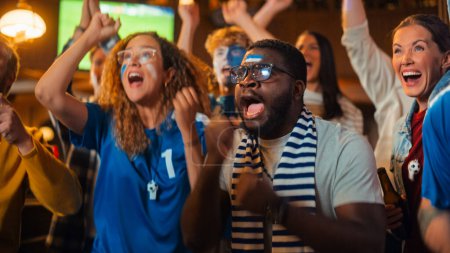 Gruppe multiethnischer Freunde, die in einer Sportbar ein Live-Fußballspiel im Fernsehen verfolgen. Fans mit aufgemalten Gesichtern jubeln. Junge Leute feiern im Team