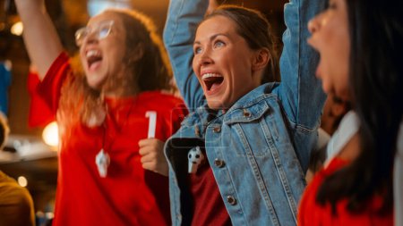 Drei Freundinnen verfolgen in einer Sportbar ein Fußballspiel live im Fernsehen. Fröhliche Mädchen jubeln und schreien. Junge Fans feiern, wenn Team ein Tor erzielt