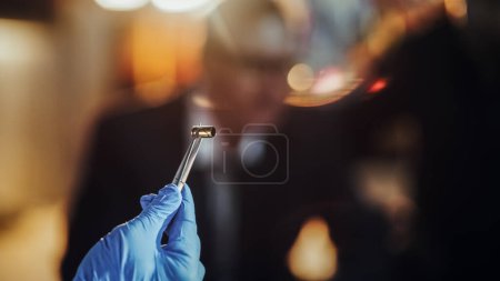 Extreme Close Up with Blurry Background: Hand with Medical Glove Using Tweezers to Hold a Bullet Shell. Forensics Specialist Finding Cartridge on
