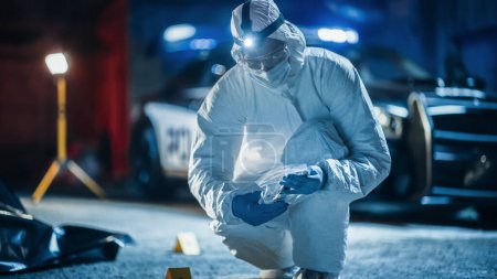 Portrait of Two Forensics Experts Doing Fieldwork at Night at a Crime Scene. One Technician Packs the Bloodied Knife as Murder Weapon While the Other