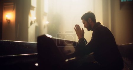Junger Christ sitzt fromm in majestätischer Kirche, mit gefalteten Händen nach einem Kreuzgebet. Er sucht Orientierung durch Glauben und Spiritualität. Religiöse