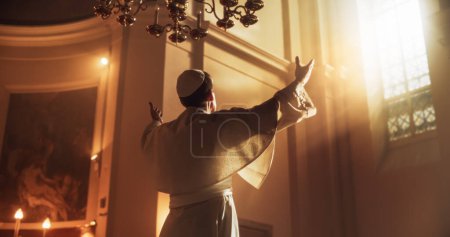 El Papa levanta las manos en un gesto de bendición universal, elevándolas hacia el cielo como señal de una devoción total a Dios. Vestido de blanco