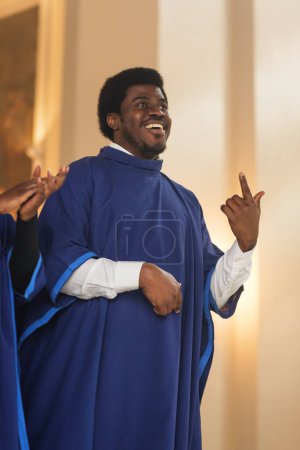 Porträt eines fröhlichen Afroamerikaners in blauer Robe in der Sonntagskirche. Black Christian Male Gospel Sänger singen und klatschen, glücklich zu sein