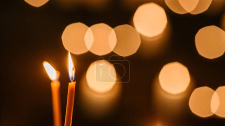 Filmaufnahmen von brennenden Kerzen auf schwarzem Hintergrund mit Bokeh-Lichtern. Warme ästhetische Atmosphäre, die Hoffnung und Frieden repräsentiert. Kerzen