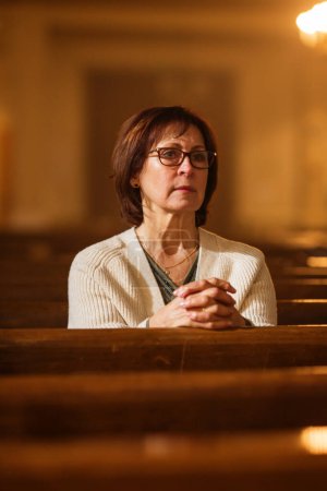 Eine fromme Seniorin sitzt fromm in einer Kirche und sucht Orientierung in ihrem religiösen Glauben und ihrer Spiritualität. Geist des Christentums und Glaubens