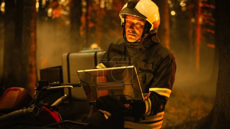 Portrait of a Handsome Fireman in Safety Gear Using Heavy-Duty Laptop Computer, Reporting on a Situation with a Dangerous Wildland Fire in a Forest