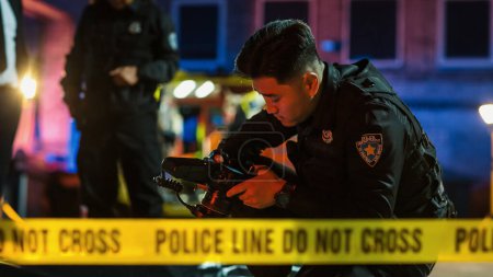 Polizist bei der Überprüfung einer Kamera nach der Aufnahme gerichtsmedizinischer Beweisfotos am Tatort. Junger Polizist hinter gelbem Klebeband
