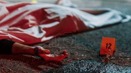 Fermer Angle bas : un cadavre avec une main sanglante posée sur le sol et recouverte. Affaire de meurtre horrible laissant la victime pour morte. Lunettes et sang marqués