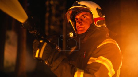 Nahaufnahme eines erfahrenen Feuerwehrmannes beim Löschen eines Wildlandbrandes tief im Wald. Profi-Trupp in Schutzanzügen und Helmen mit Feuerwehrschlauch