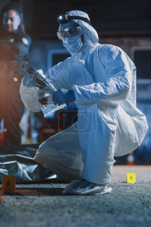 Faible, tir au sol : Forensics in Coverall costume marche vers des preuves sur une scène de crime et emballage de l'arme de meurtre. un cas choquant de haine