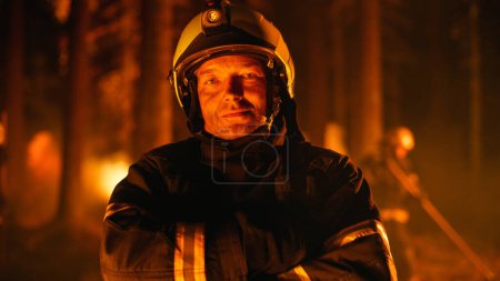 Porträt eines tapferen jungen erwachsenen Feuerwehrmannes in Sicherheitsuniform und Helm, der während eines Flächenbrandes für die Kamera posiert. Berufsfeuerwehrmann gesucht