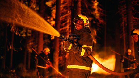 Porträt eines ansehnlichen afroamerikanischen Feuerwehrmannes, der einen Waldbrand methodisch mit Hilfe eines Feuerwehrschlauchs löscht. Feuerwehr-Rettung