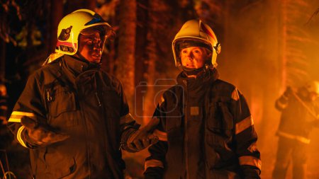 Porträt zweier Berufsfeuerwehrleute, die im Wald stehen und den Lagebericht bei einem Waldbrand diskutieren. Konzentrierte Superintendentin