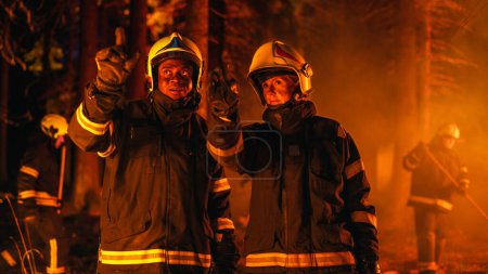 Porträt zweier Berufsfeuerwehrleute, die im Wald stehen und den Lagebericht bei einem Waldbrand diskutieren. Superintendentin im Gespräch