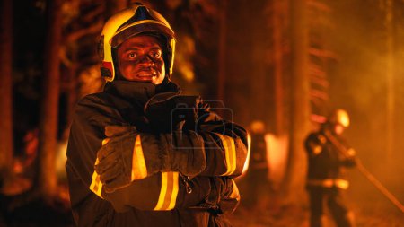 Portrait of a Black Handsome Young Adult Firefighter in Safety Uniform and a Helmet Posing for Camera During a Wildfire. Professional Fireman Looking