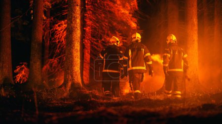 Diverse Trupps männlicher und weiblicher Feuerwehrleute sind tief in einem Wald unterwegs, um die Ausbreitung eines Waldbrandes zu verhindern. Superintendent erteilt Orden und