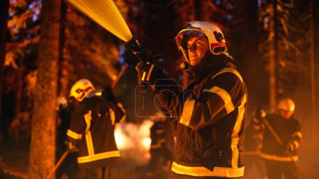 Porträt eines hübschen kaukasischen Berufsfeuerwehrmanns, der einen Waldbrand methodisch mit einem Feuerwehrschlauch löscht. Feuerwehr rettet Wildland