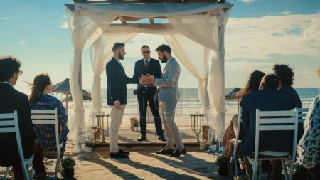Handsome Gay Couple Exchange Rings and Kiss at Outdoors Wedding Ceremony Venue Near the Sea. Two Happy Men in Love Share Their Big Day with Diverse