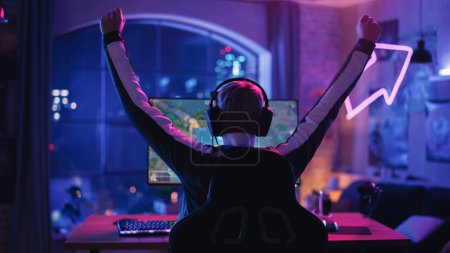 Jeune joueuse qui réussit à porter un casque et à gagner dans un jeu vidéo sur un ordinateur personnel dans un salon lumineux au néon à la maison. Soirée confortable à