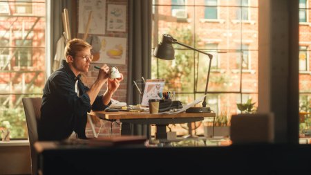Junger männlicher Künstler arbeitet an maßgeschneiderten Turnschuhen vor seinem Laptop im Creative Loft Office Space. Mann mit weißen Schuhen. Trendig