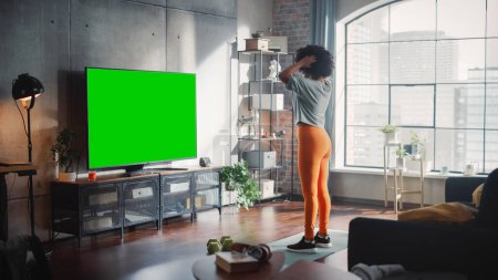 Gimnasio en casa: Gorgeous Positive Black Girl Entrenamiento con el uso de pantalla verde Mock-up TV. Mujer auténtica utiliza la aplicación de fitness de entrenamiento, Streaming Virtual